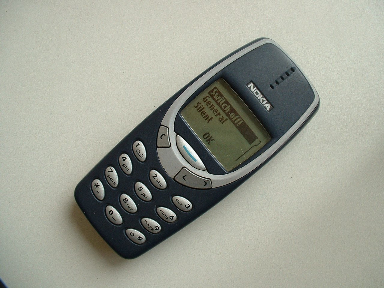 a cellphone sits on a white surface and displays the time