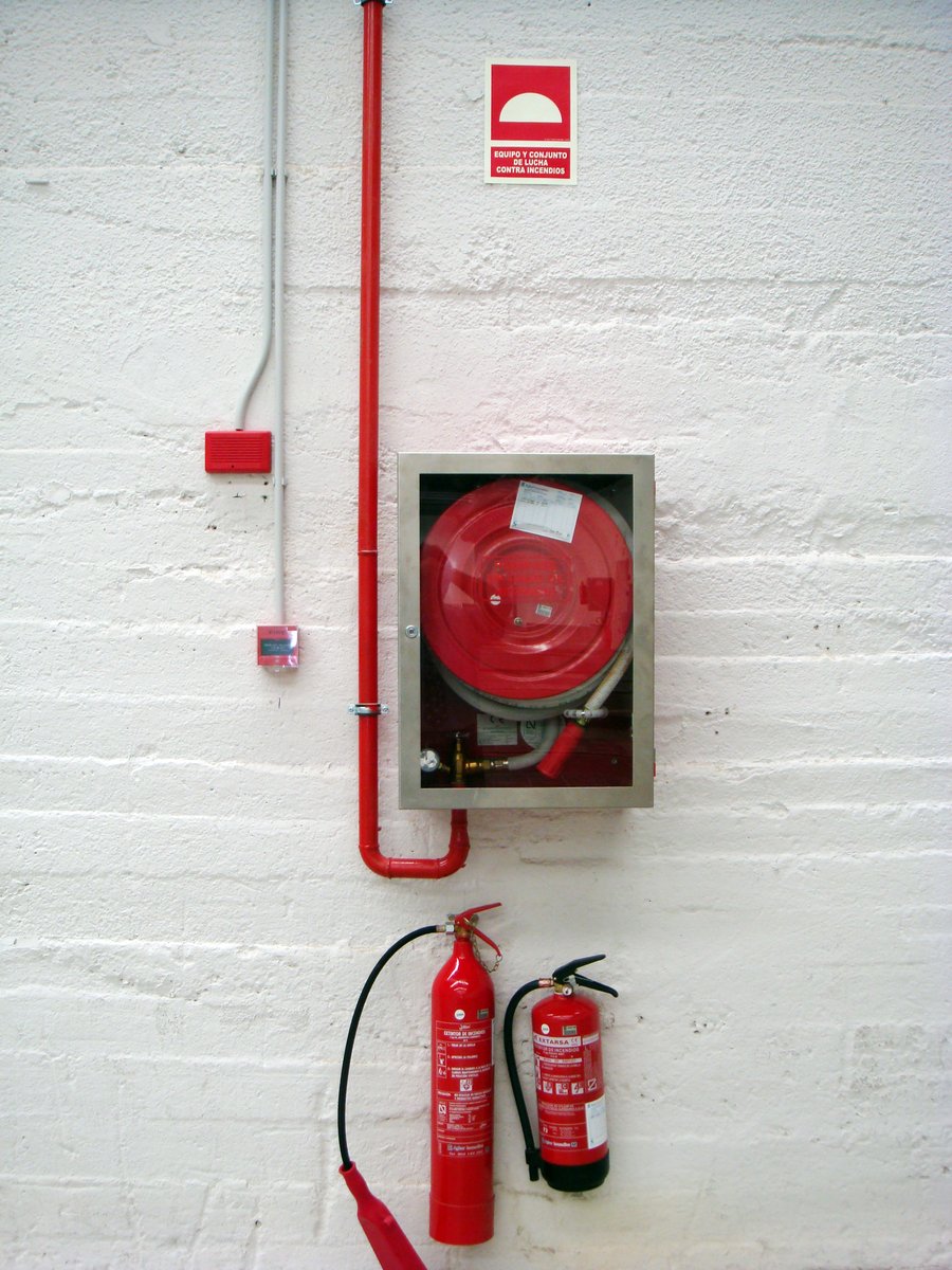a red fire hydrant and two fire extinguishers sitting on top of a white brick wall