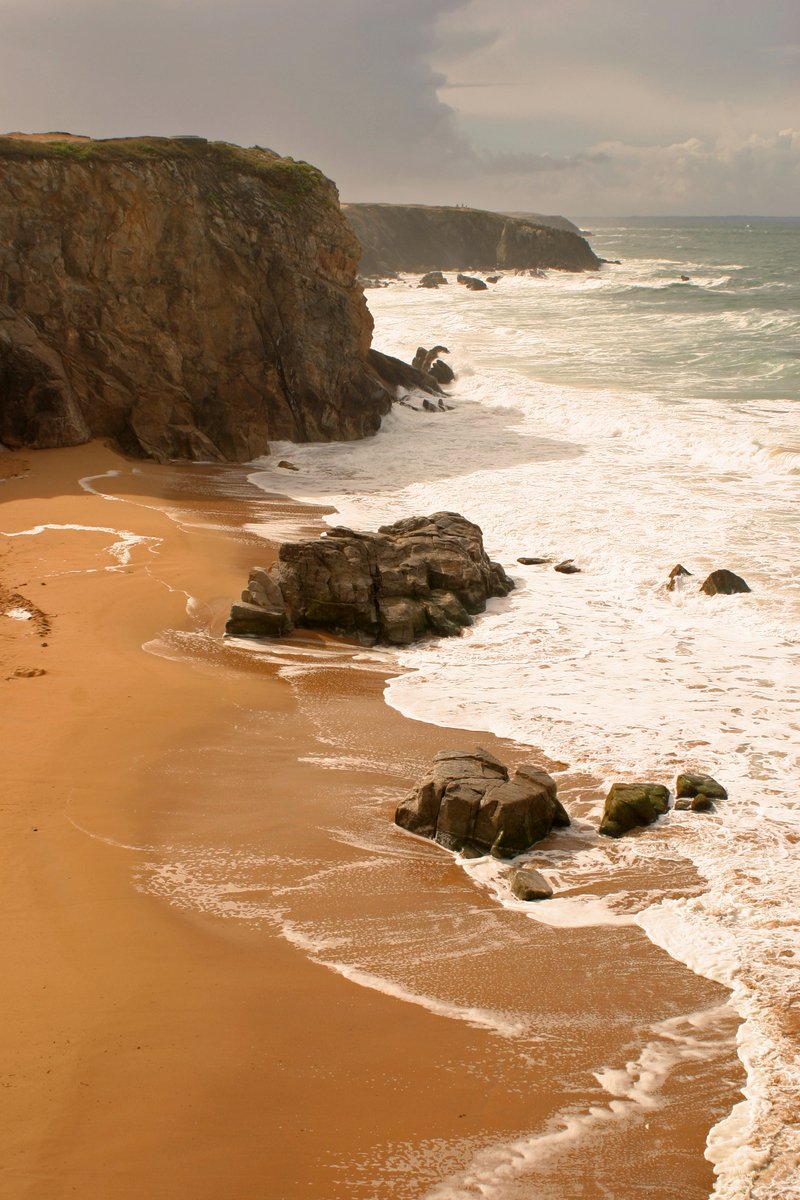 a beach with brown and green colored sand near the ocean