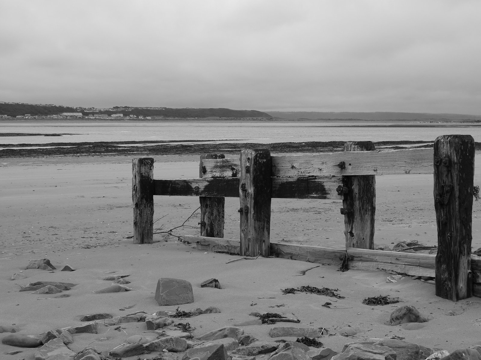 a fence with broken posts stands on sand near the water