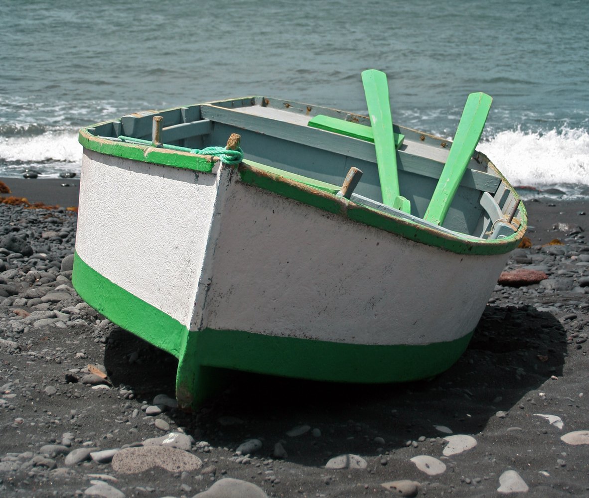 a green and white boat sits on a rocky beach