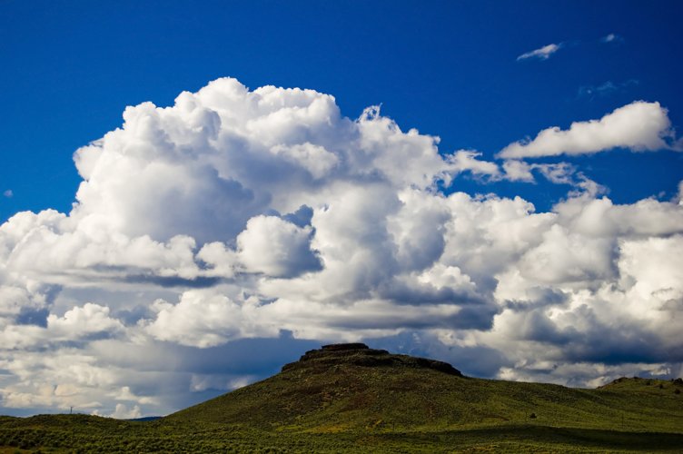 large cums are forming clouds in the sky on a grassy hill