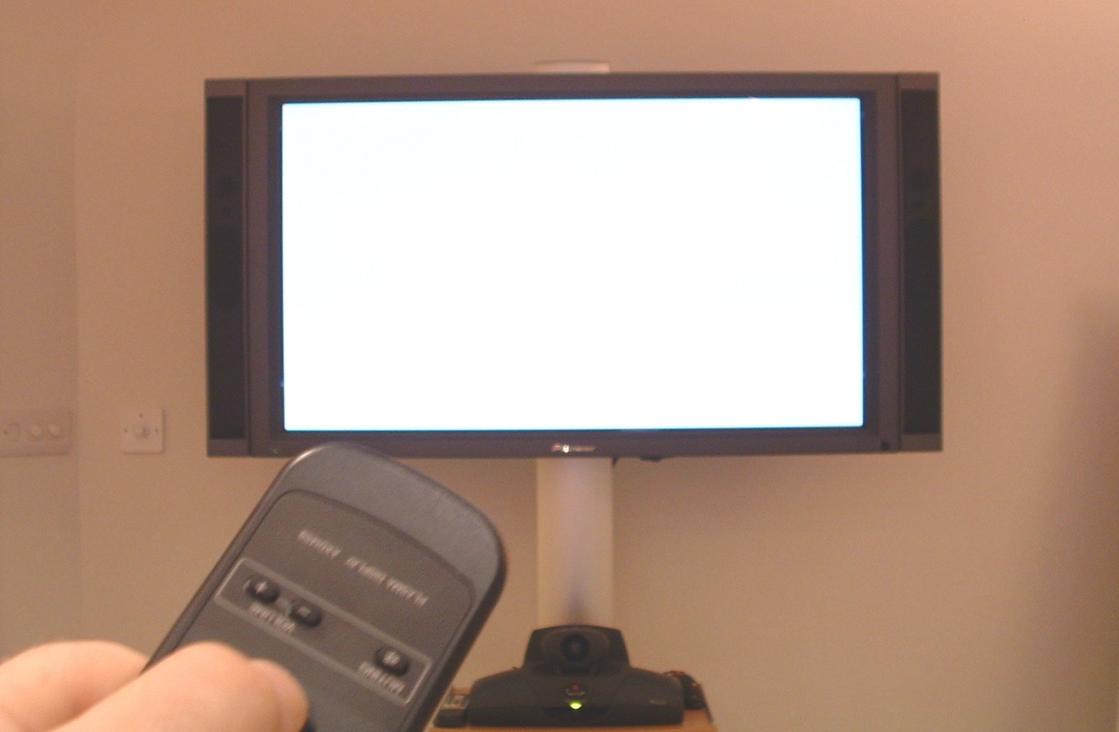 hand holding a remote control pointed at a flat screen television