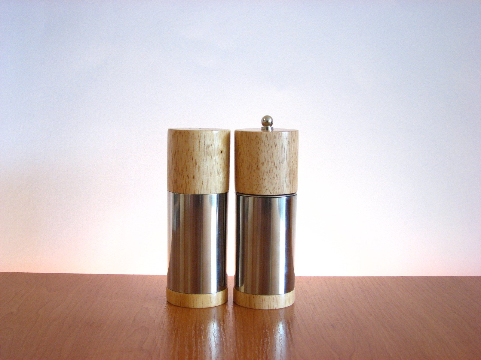 two metal containers on a wooden table with a beige wall behind them