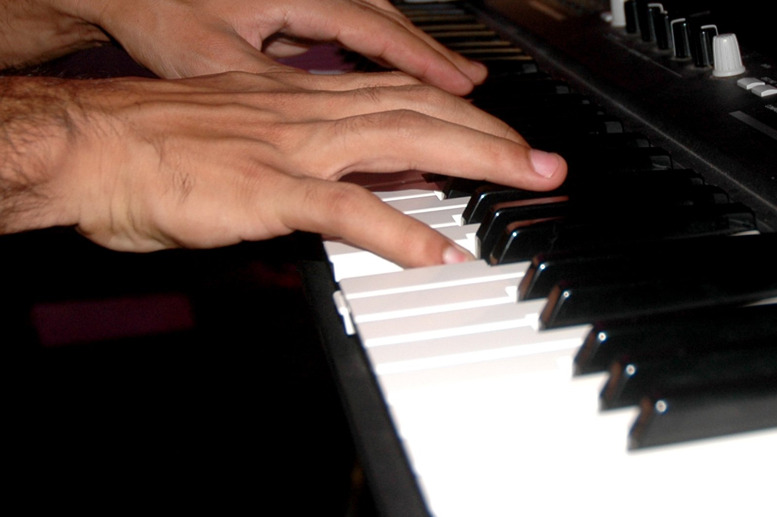 one hand plays the piano while another hand rests on it