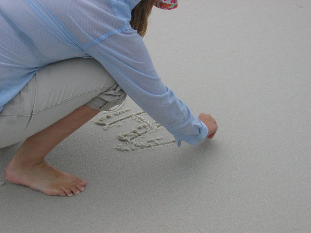 there is a woman crouched down writing in the sand