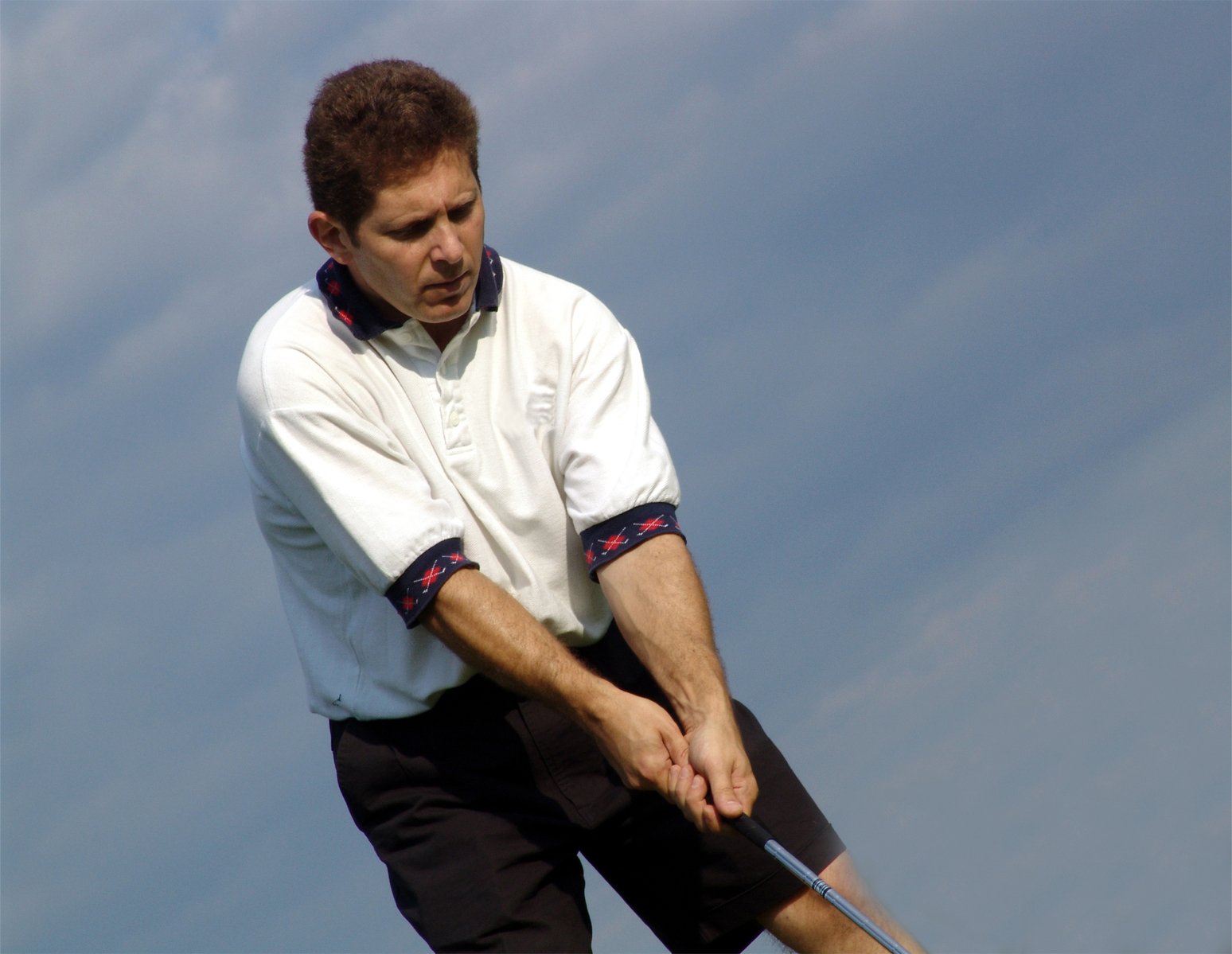 a man swinging a golf club in front of blue skies