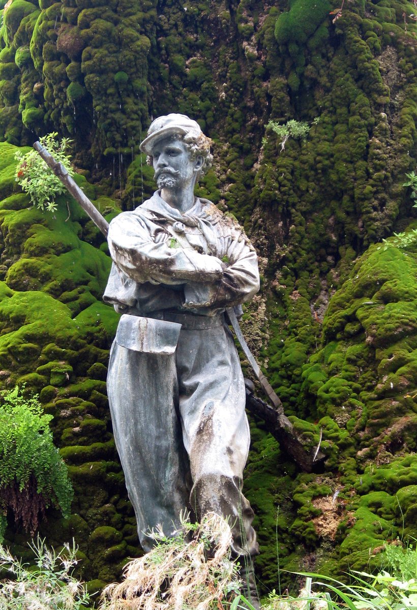 the statue is posed near the moss covered mountain