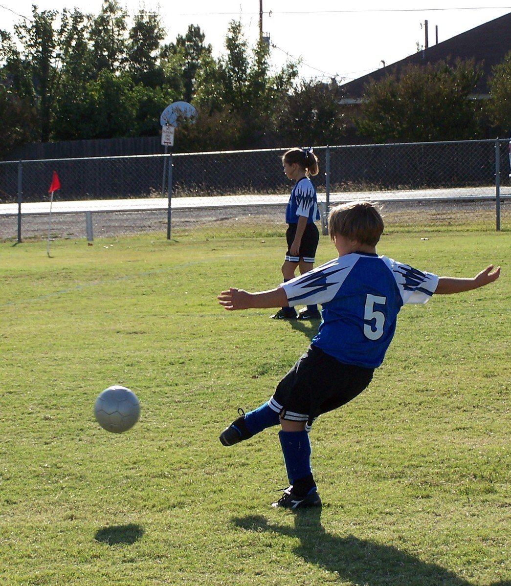 a boy is playing soccer while another  watches