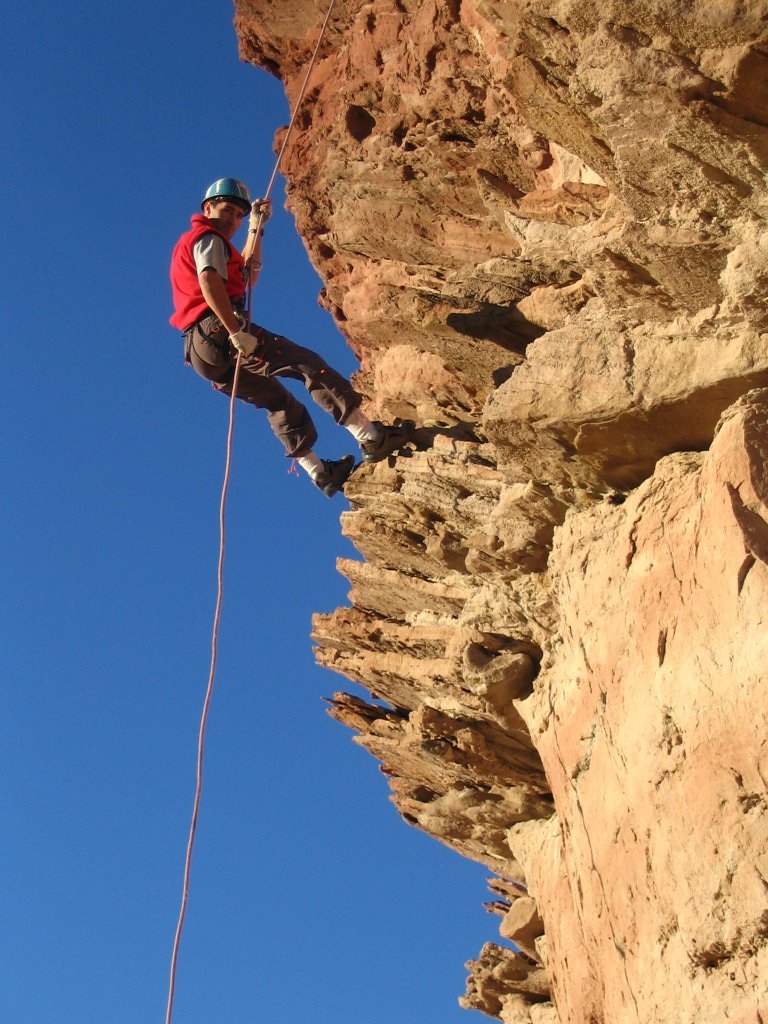 man with helmet and safety gear climbing up a cliff
