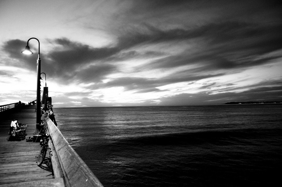 an empty pier with benches on the sides of the boardwalk and a bright light in the background