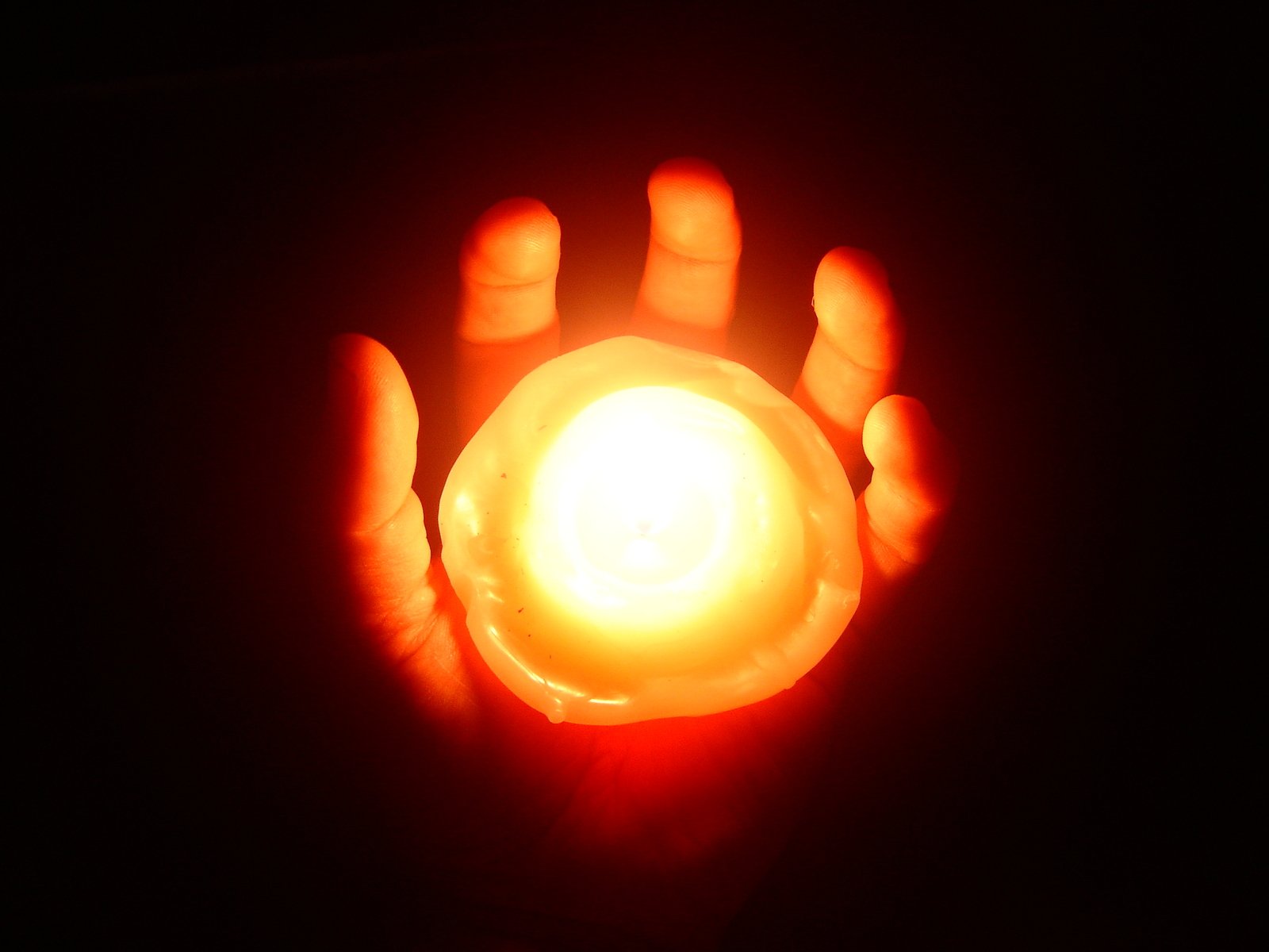 hands holding a candle on black background in darkness