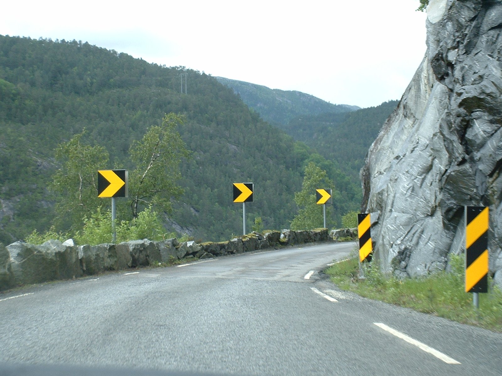 several yellow traffic signs on a mountain road