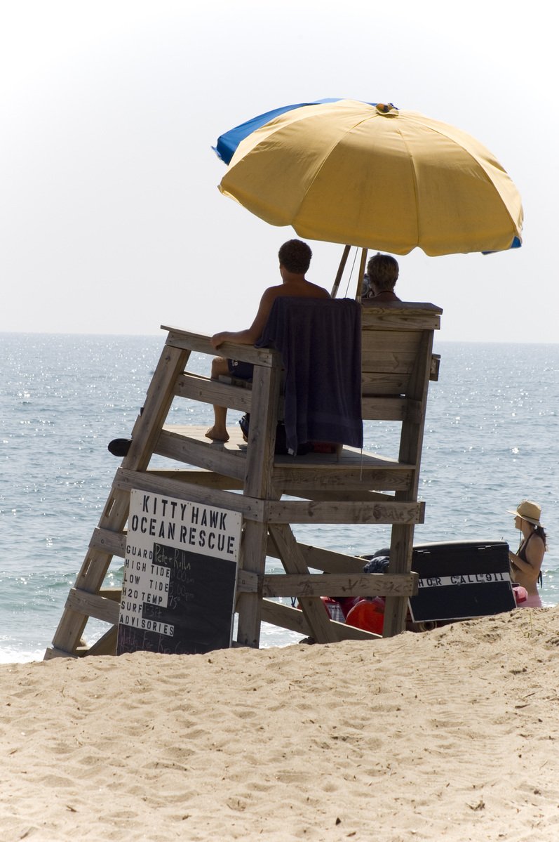 three people on a life guard bench at the beach