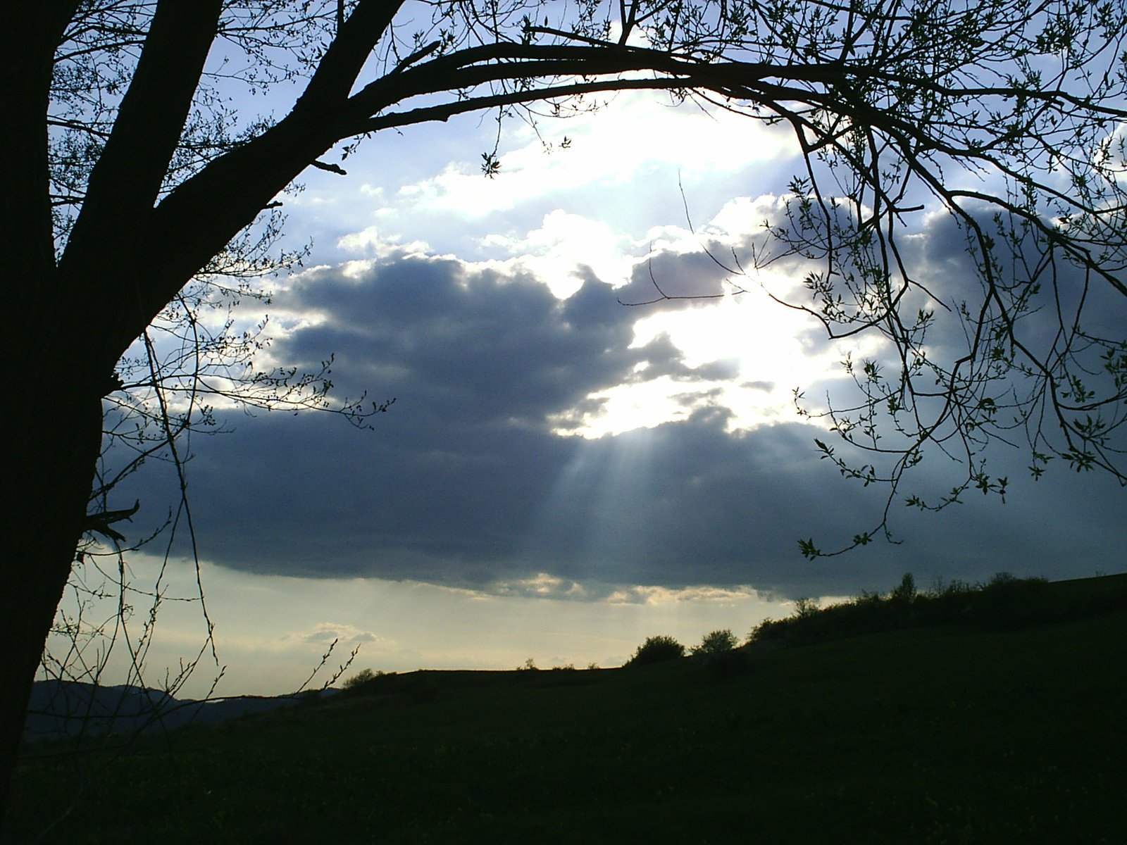 sun shining through clouds over a hill and grassy field