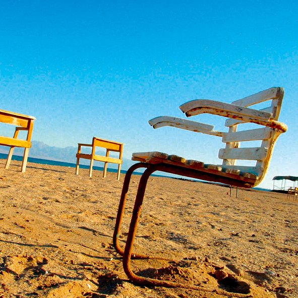 the two chairs are on the sand by the water