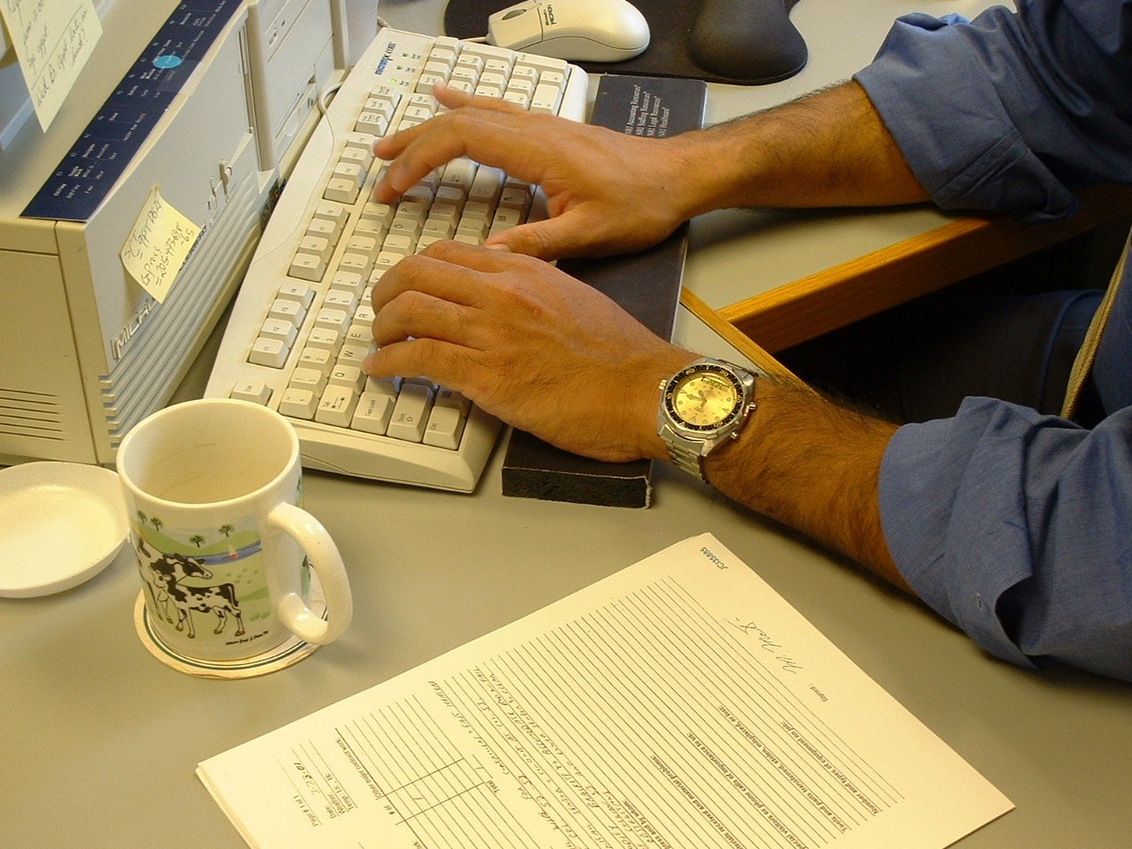 a man is typing on his computer with a cup