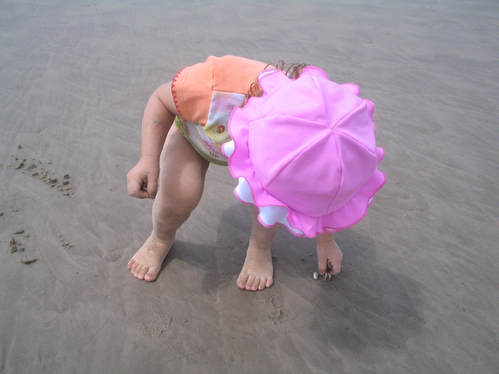 a little girl on the beach has a pink umbrella