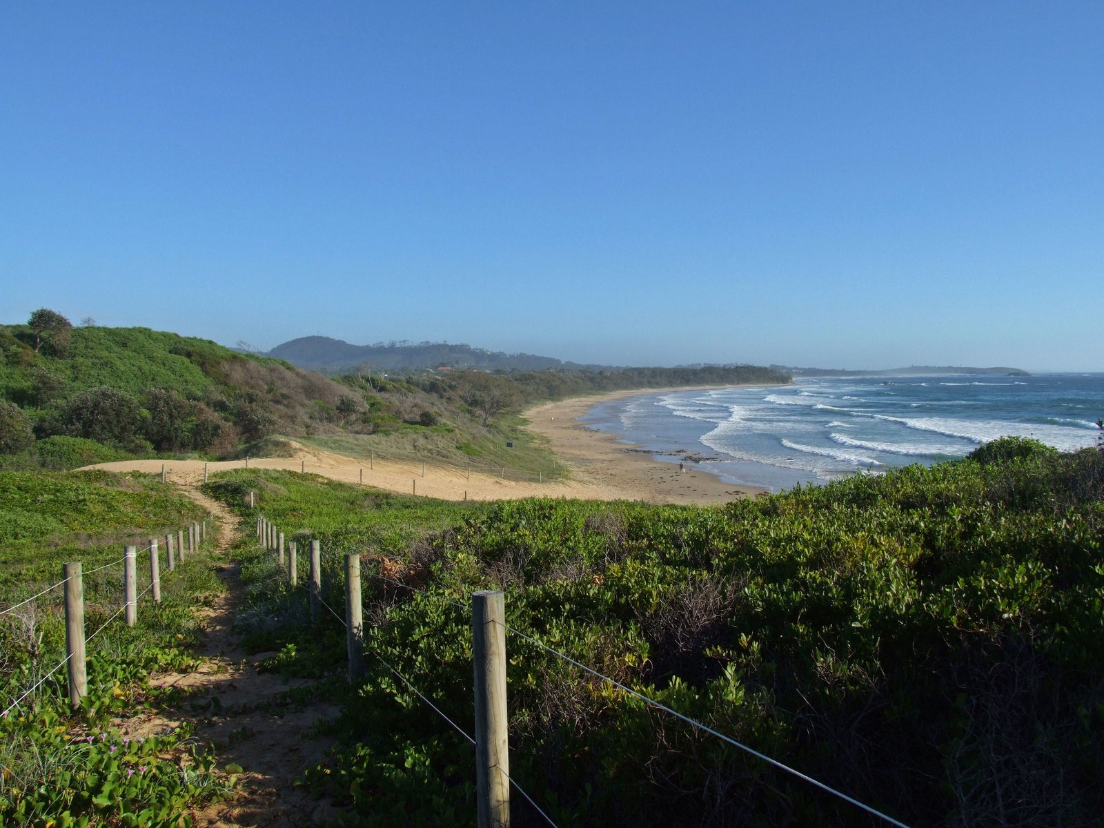 a beach next to the ocean with a fence going into it