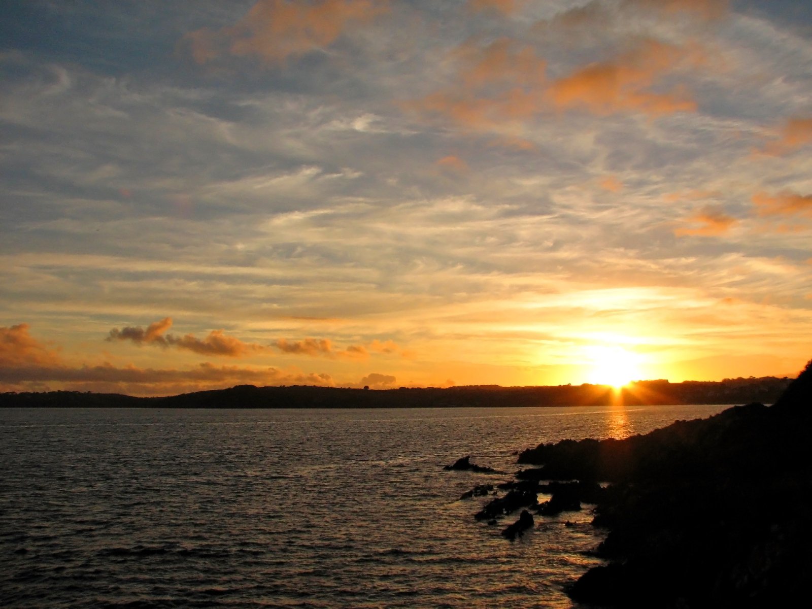 a sunset over the water with clouds and a small island