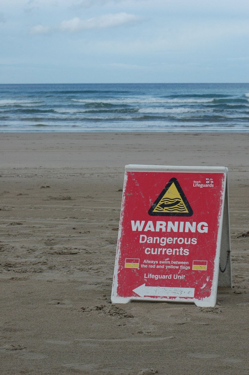 a warning sign on the beach stating dangerous currents