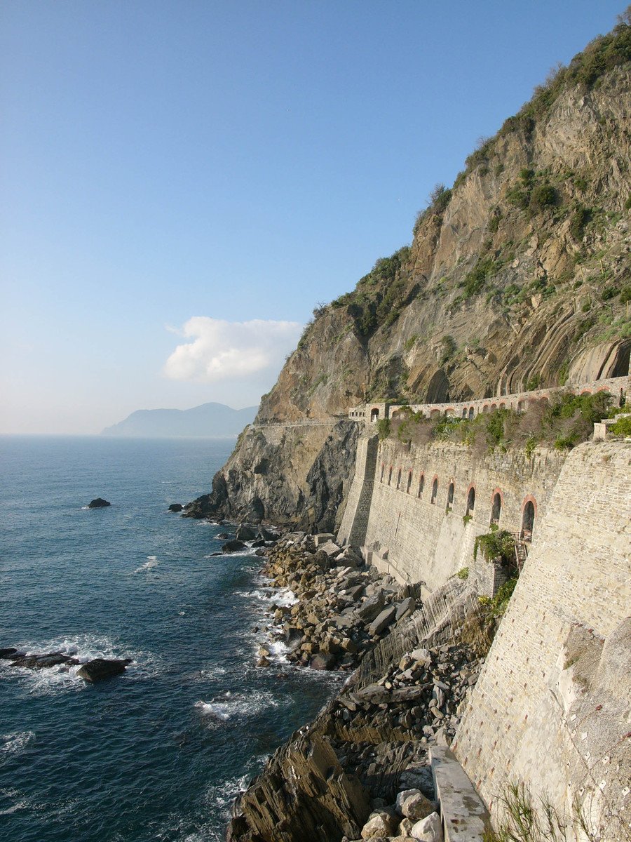 people are walking along the ocean beside a rocky cliff