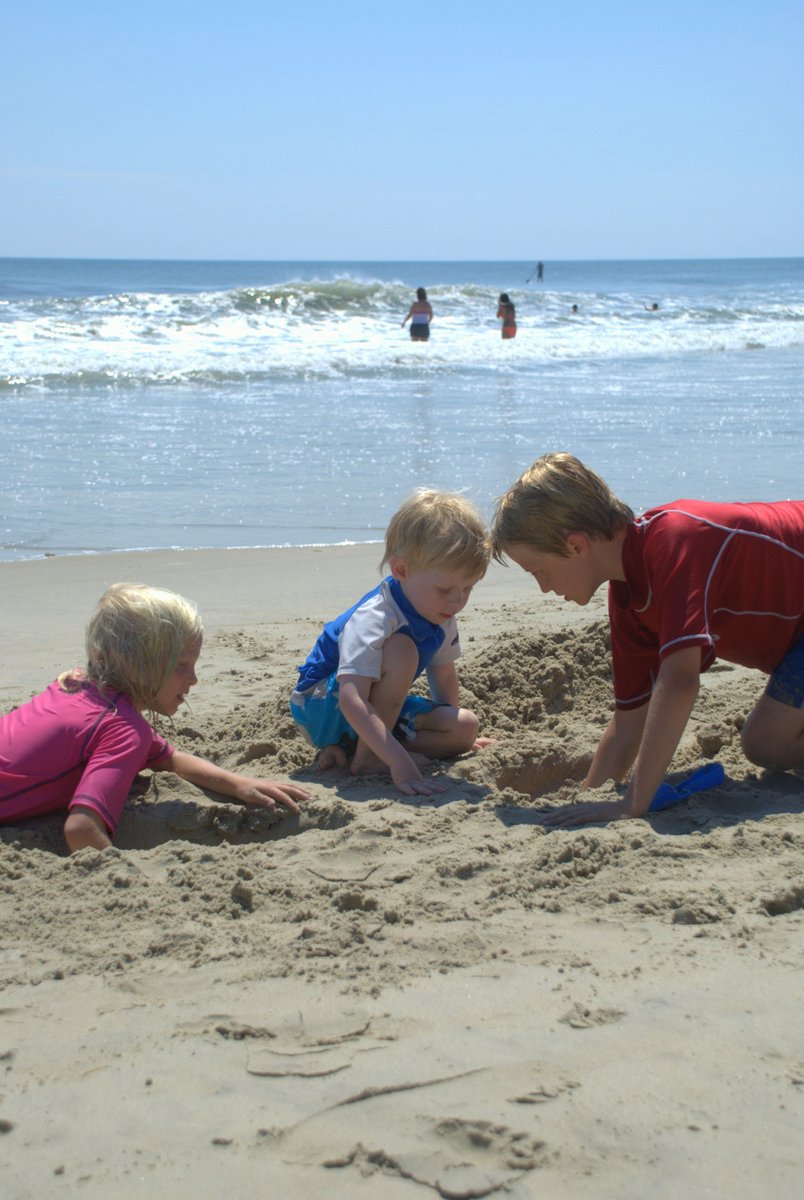 three young children play with their toys on the beach