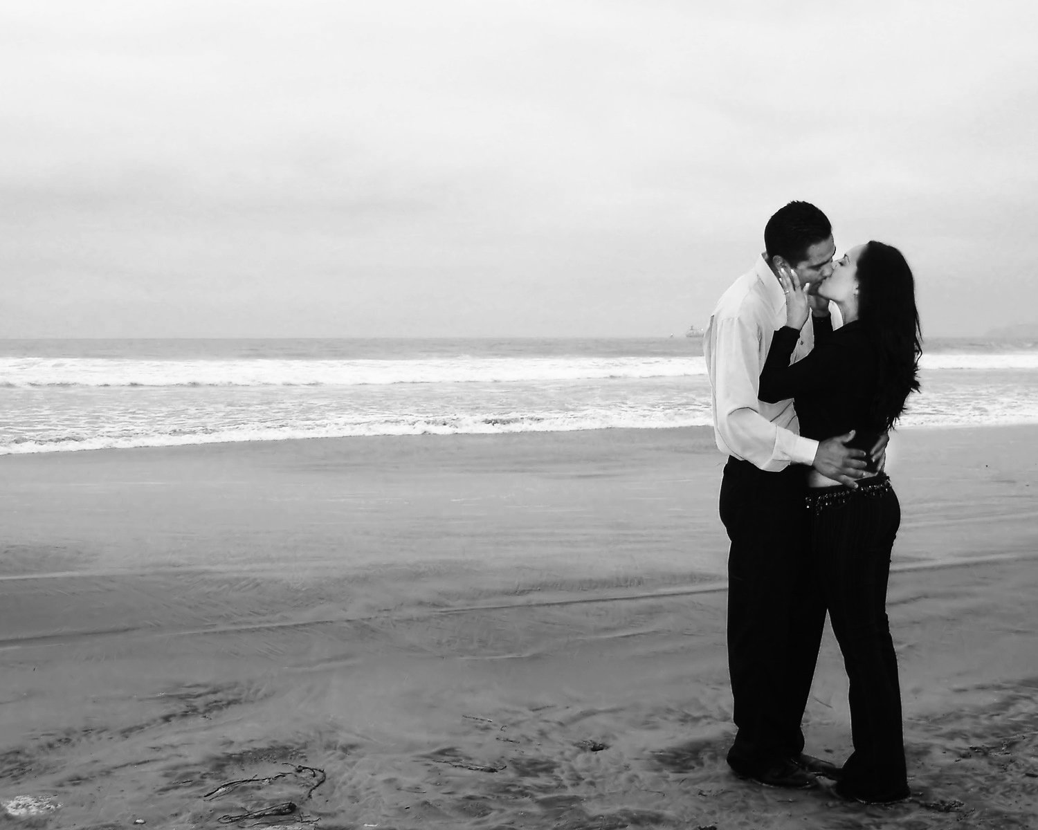 two people kissing on the beach on an overcast day