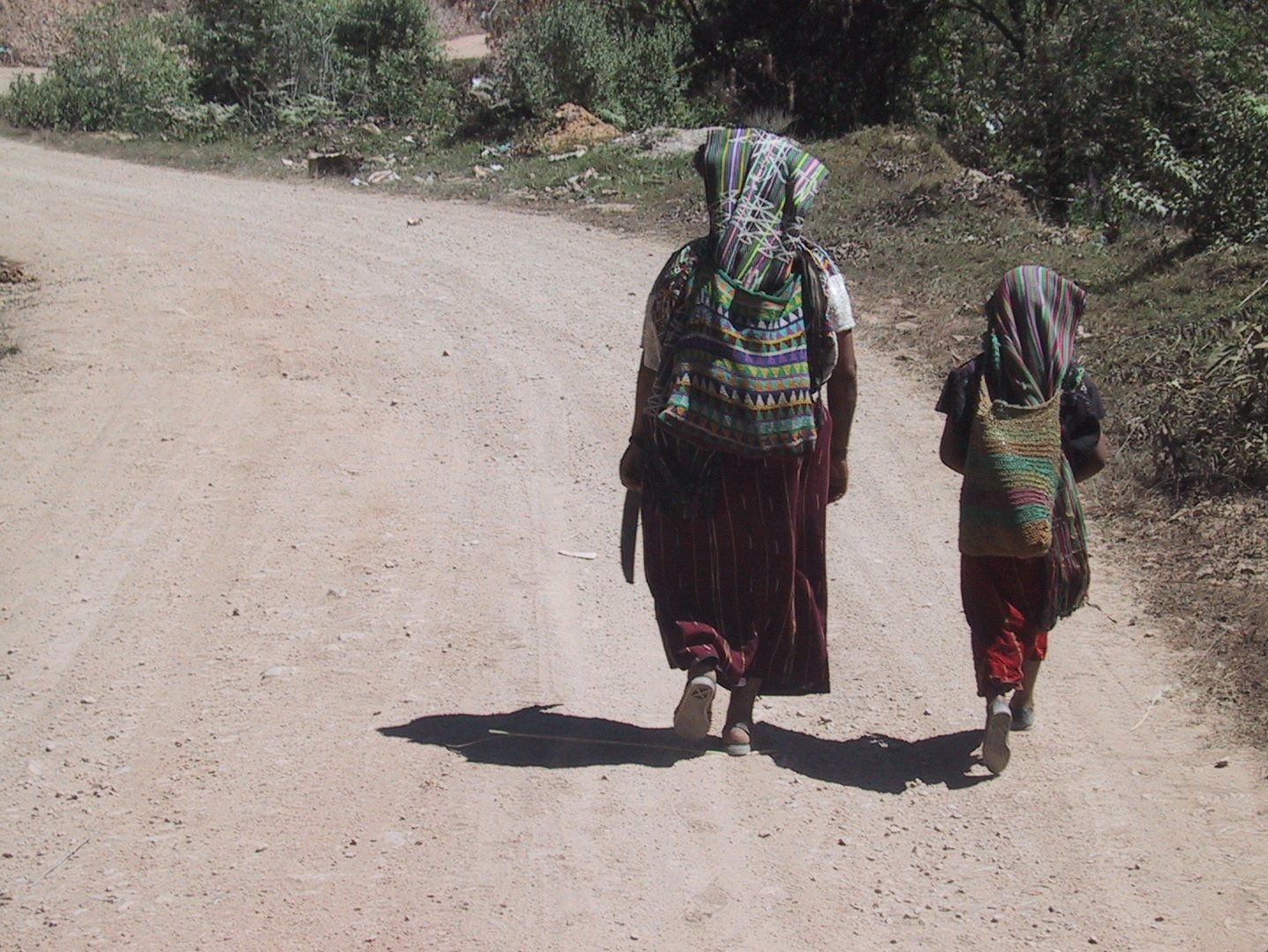 two women walk down a dirt road wearing colorful clothing