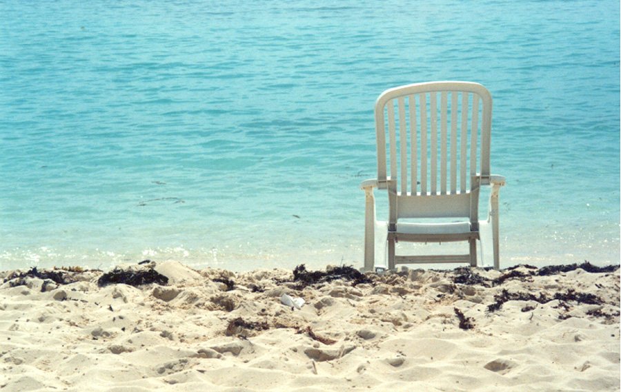 a beach with a lawn chair in the sand and an ocean behind it
