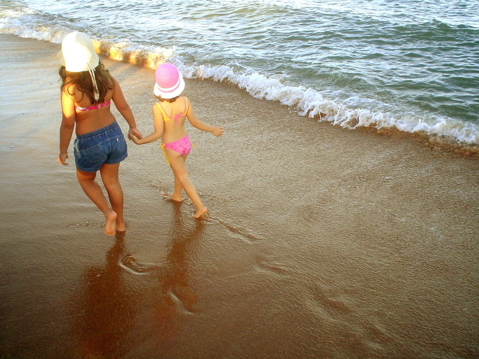 two children wearing sun hats are running along the beach