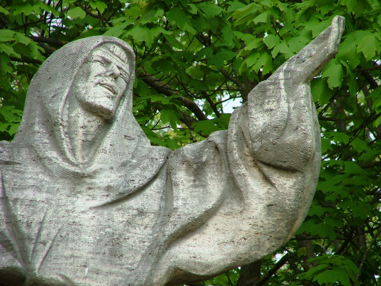 a stone statue of a person with a hood is in the middle of some nches