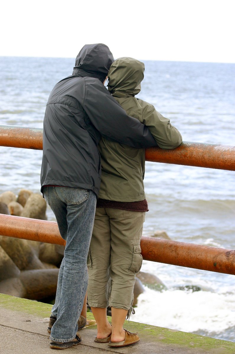 the man and woman is hugging against the railing next to the water