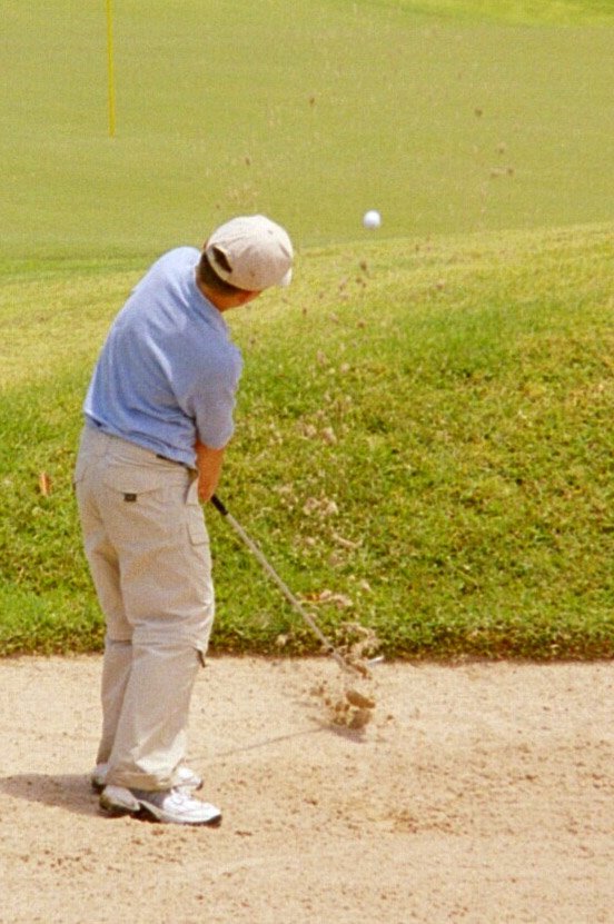 a man hitting a golf ball with a club on a dirt course