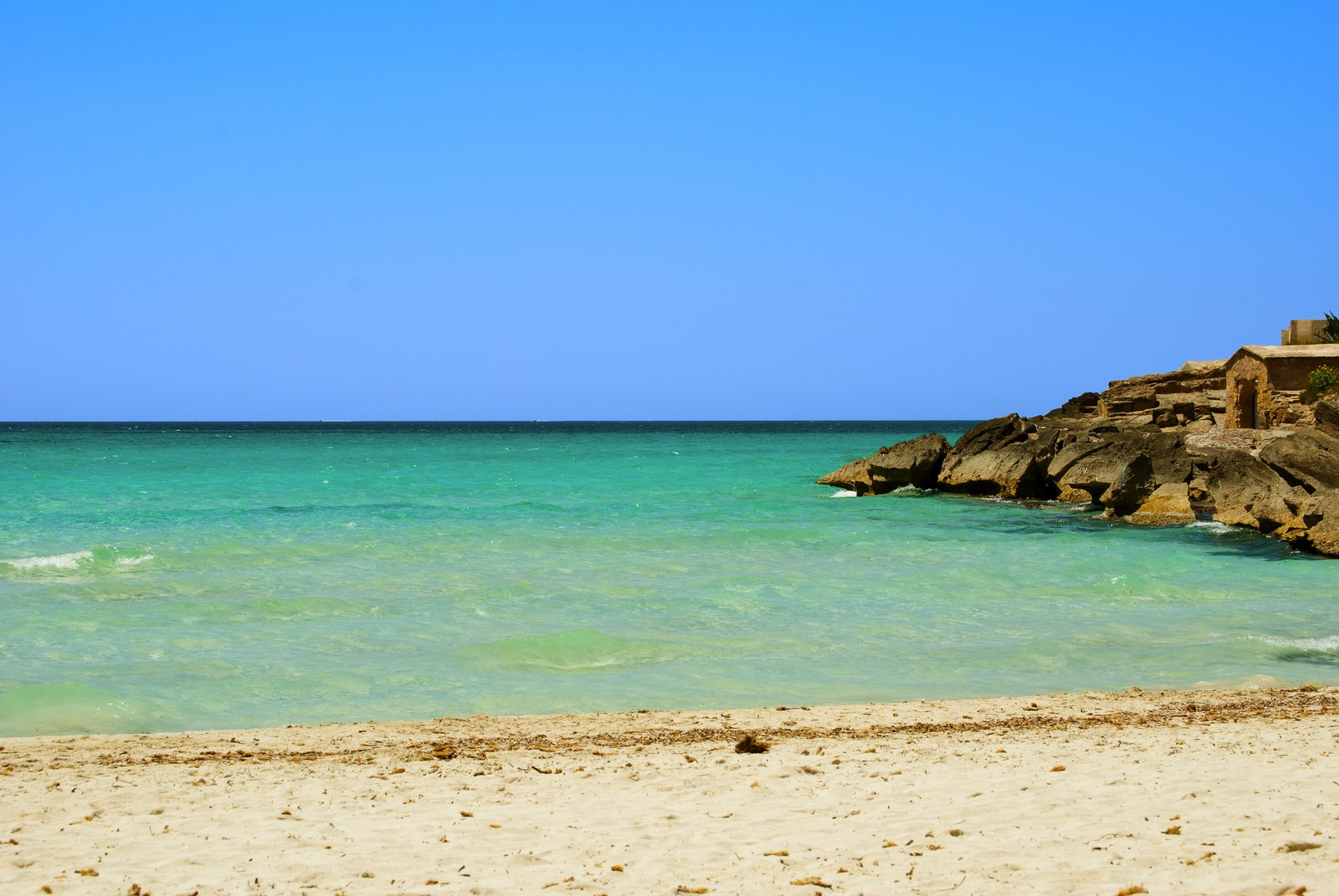 a beach scene with a person sitting on the edge of the ocean and a building in the distance