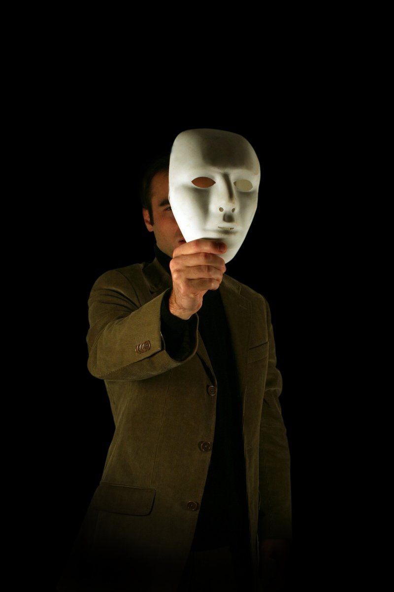 man holding mask while making hand gesture on dark background