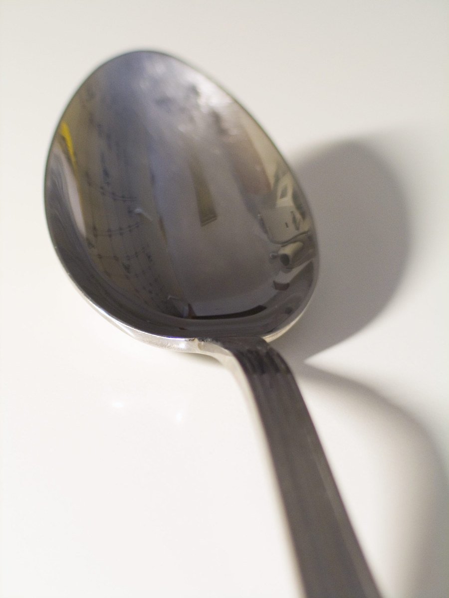 a spoon with a reflection of itself on a white surface