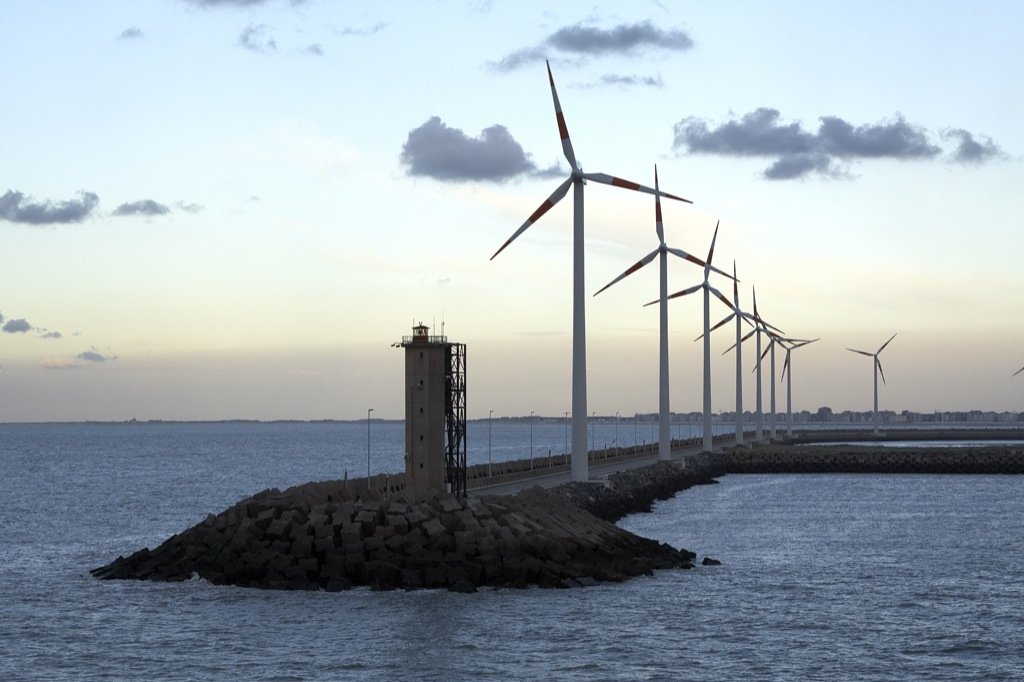 windmills along a sea wall and walkway in the sunset