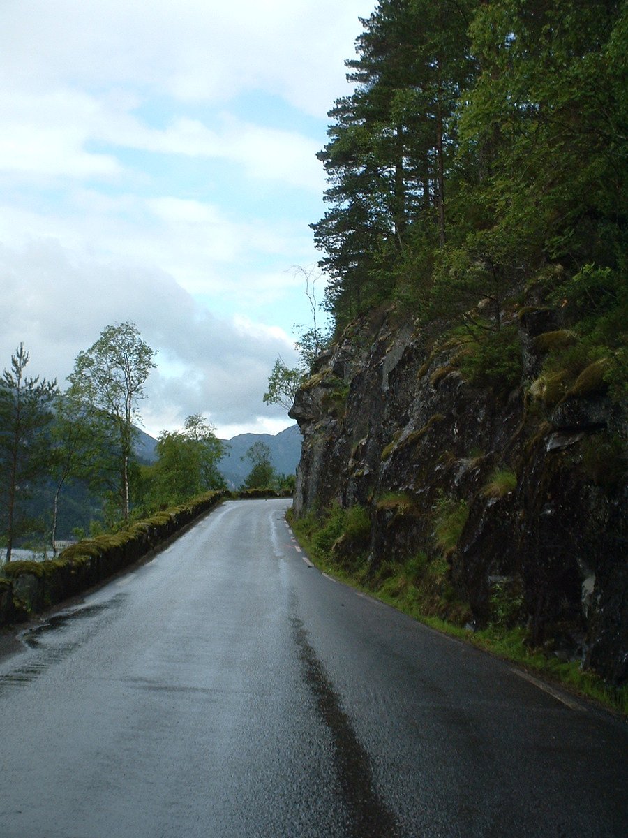a view of a narrow paved road with a rock wall in the distance
