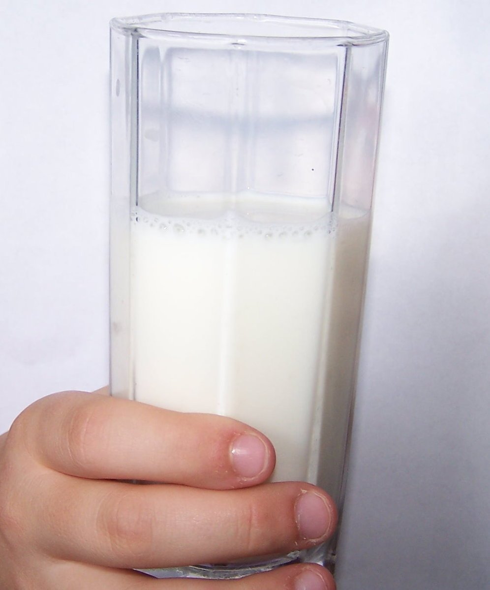a close up of a person holding a tall glass of milk