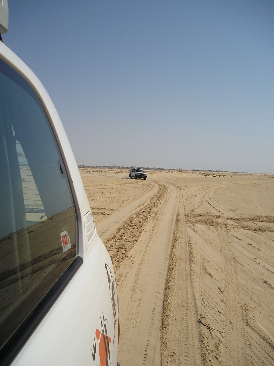 a white truck and vehicle driving on desert dirt