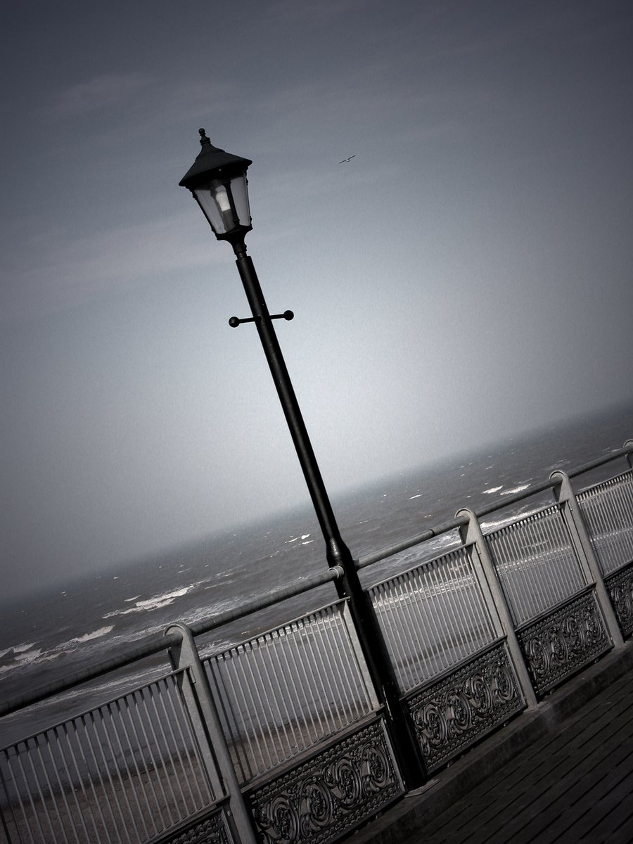 a long, dark street light is on a very high pier