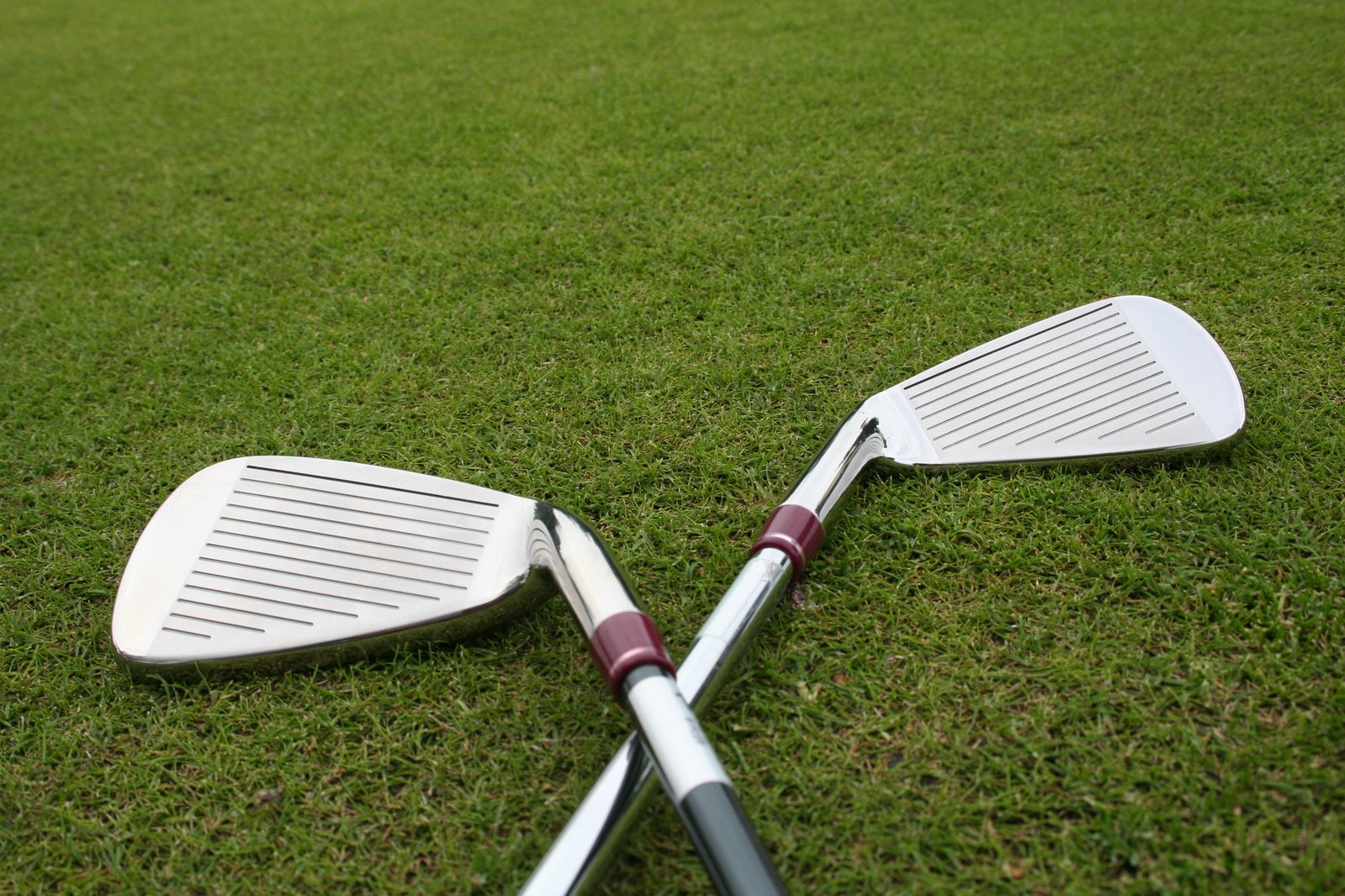 two white golf bats on the grass next to two red handled irons