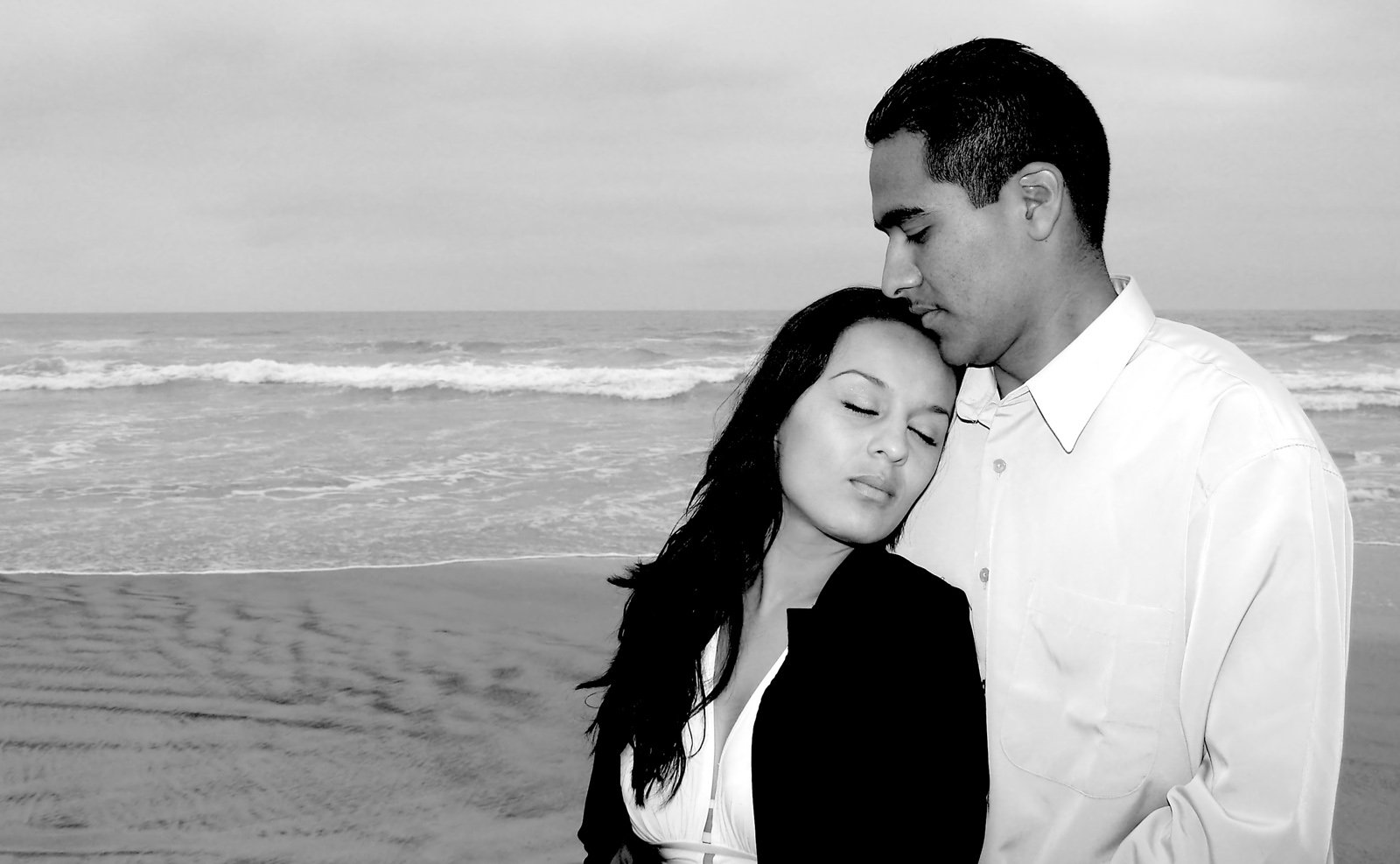 a couple cuddles close while standing on the beach