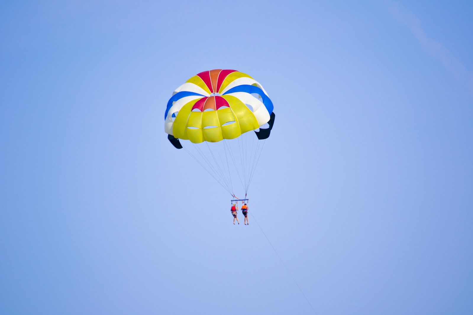 the person in red, white and blue is parasailing through the clear sky