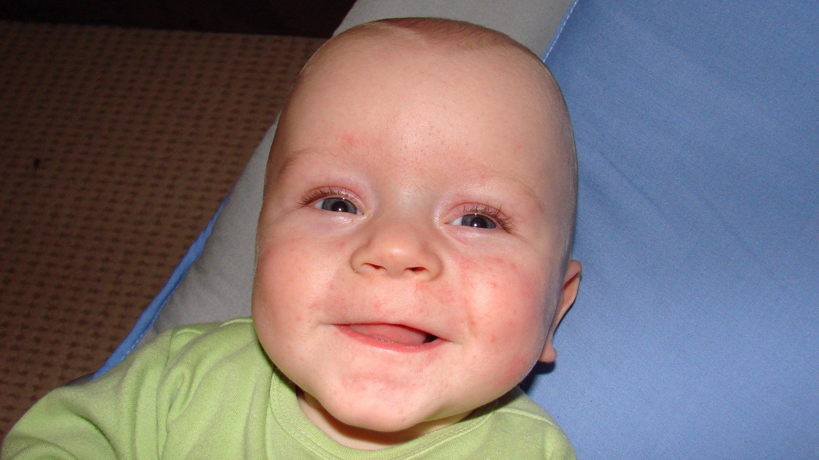 an infant boy wearing a green shirt and smiling