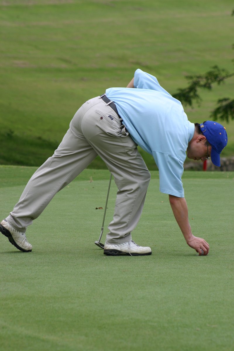 a man wearing blue shirt and grey pants bending over playing golf