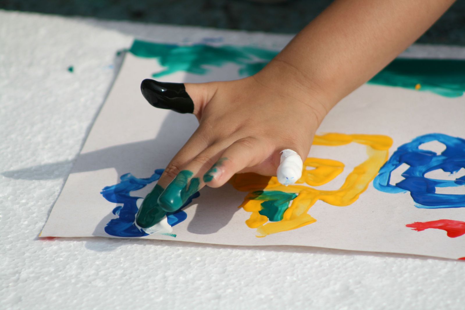 a child's hand with a paintbrush on a white paper