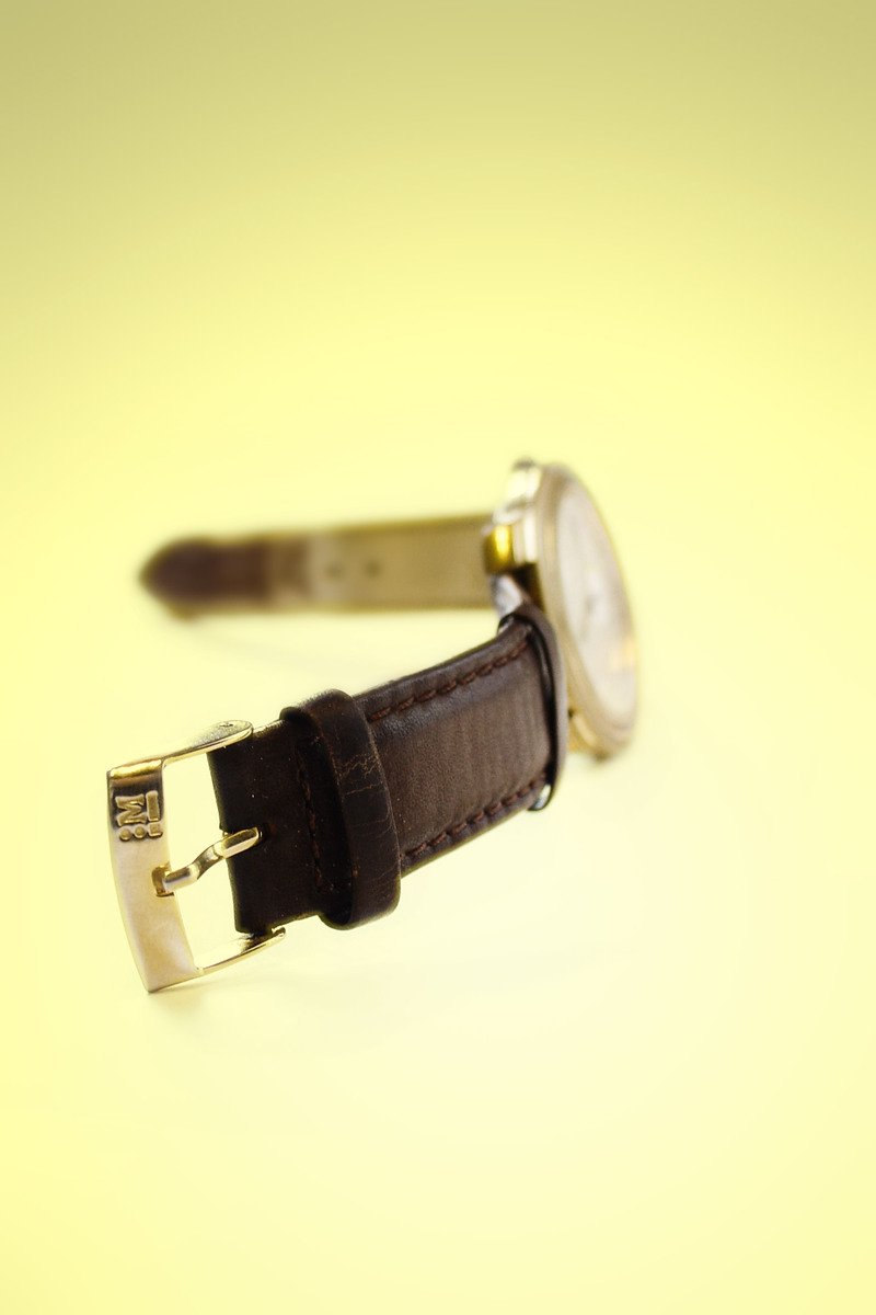 the gold plated wrist watch is next to a brown strap