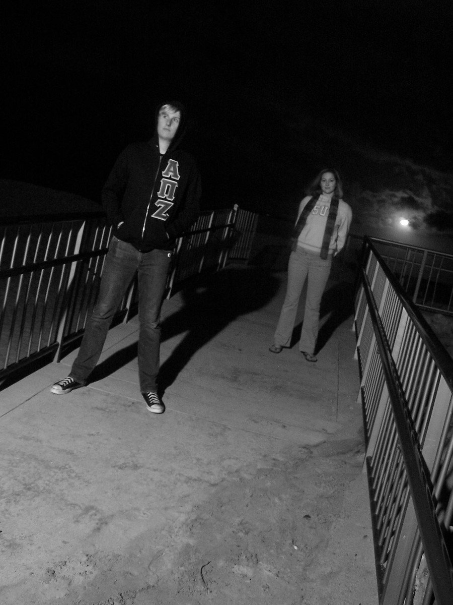 two men standing near a fence and rail at night